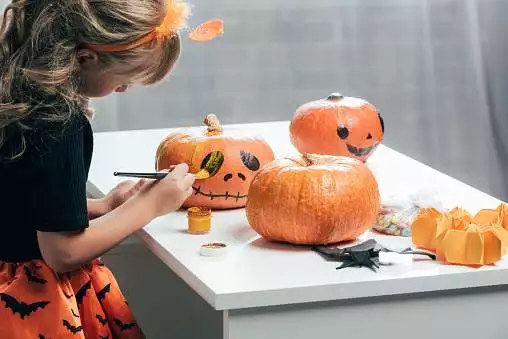 side view of cute child painting pumpkins for halloween at home